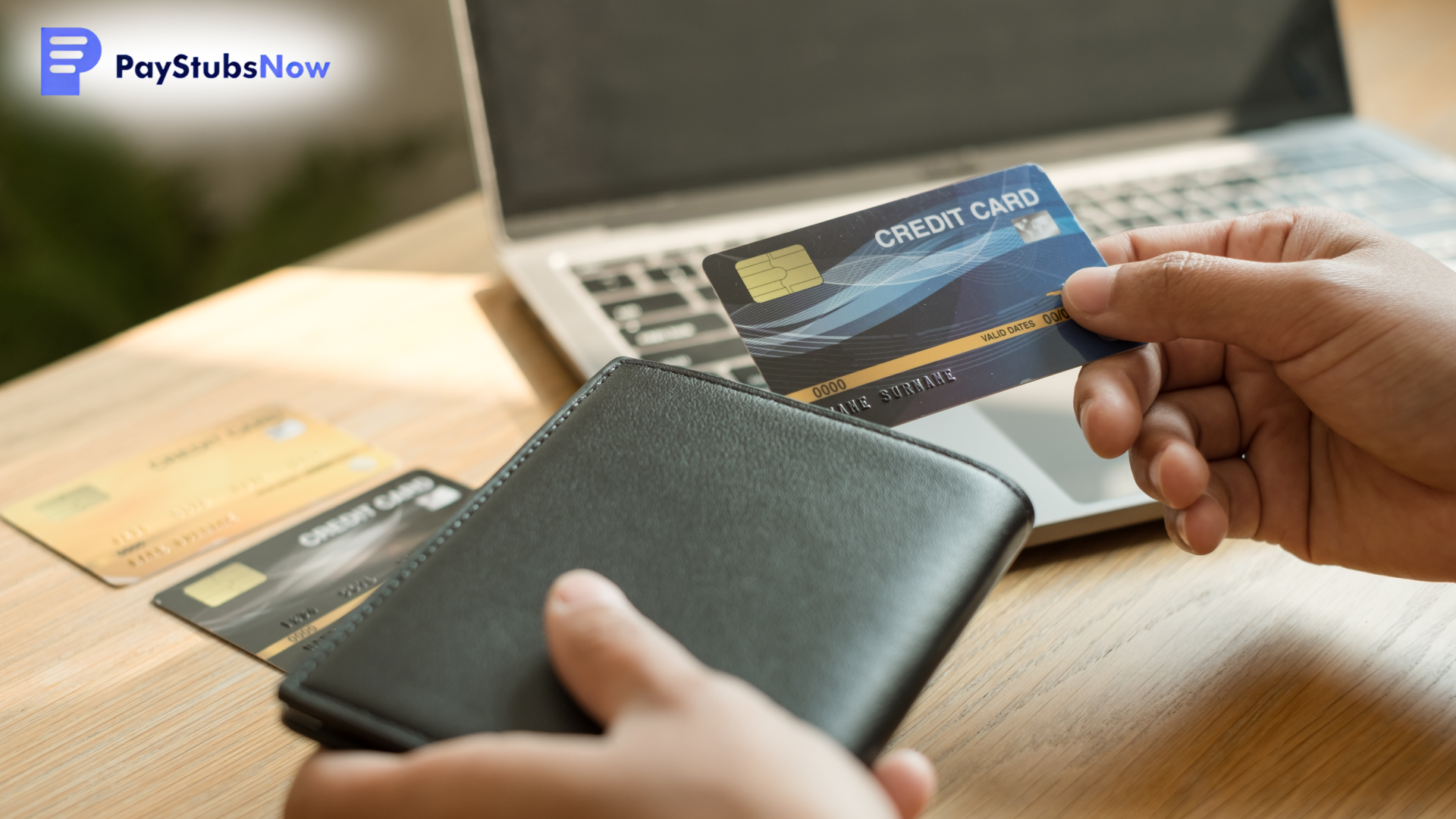 A person holds a credit card and wallet near a laptop.