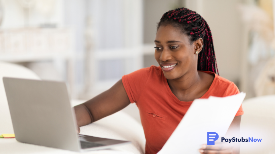 A woman holds a document while working on a laptop